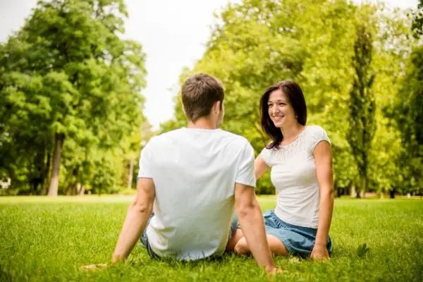 Couple talking while on the grass with trees on the background