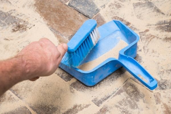 person brushing layers of sand in paver joints