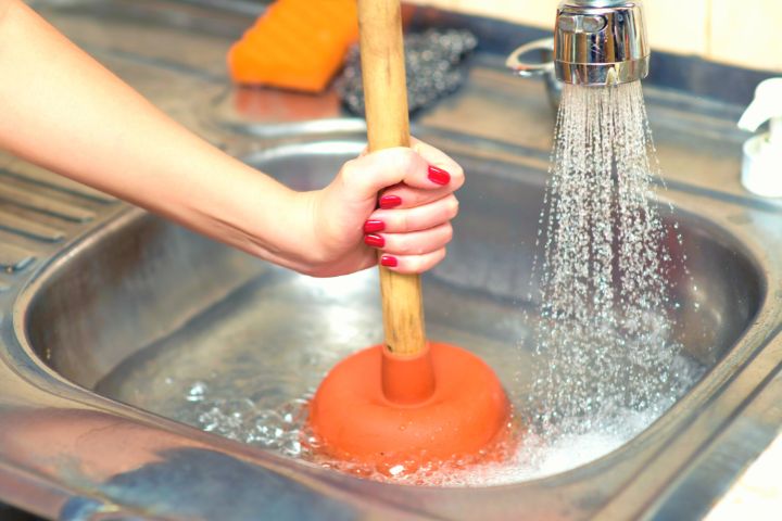 Woman With Plunger Is Removing Clog In The Sink