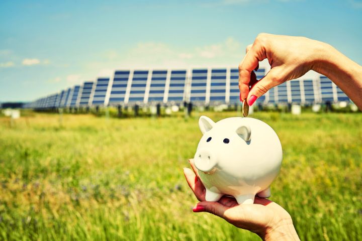 A Girl Puts A Coin In A Piggy Bank With Solar Panels On The Background