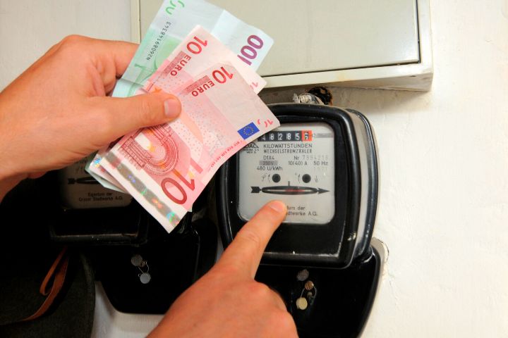 Man With Money In Hand And Finger On Electricity Meter
