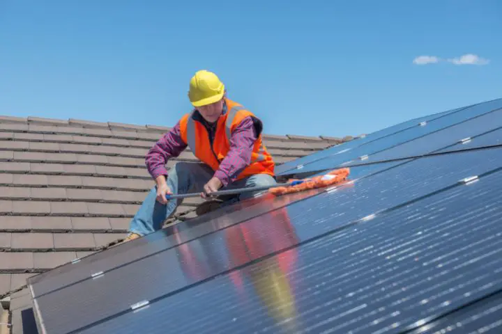 Man Is Sitting On A Roof And Cleaning Solar Panels
