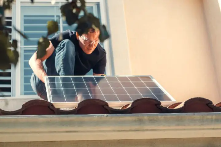 A Man In Black Shirt Installing A Solar Panel On The Roof